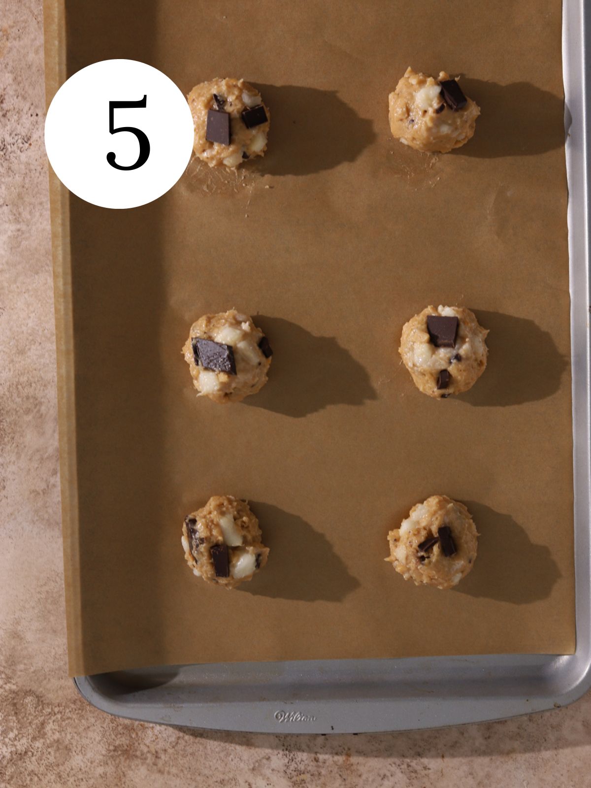 A baking sheet with parchment paper and chocolate pear cookie dough balls.