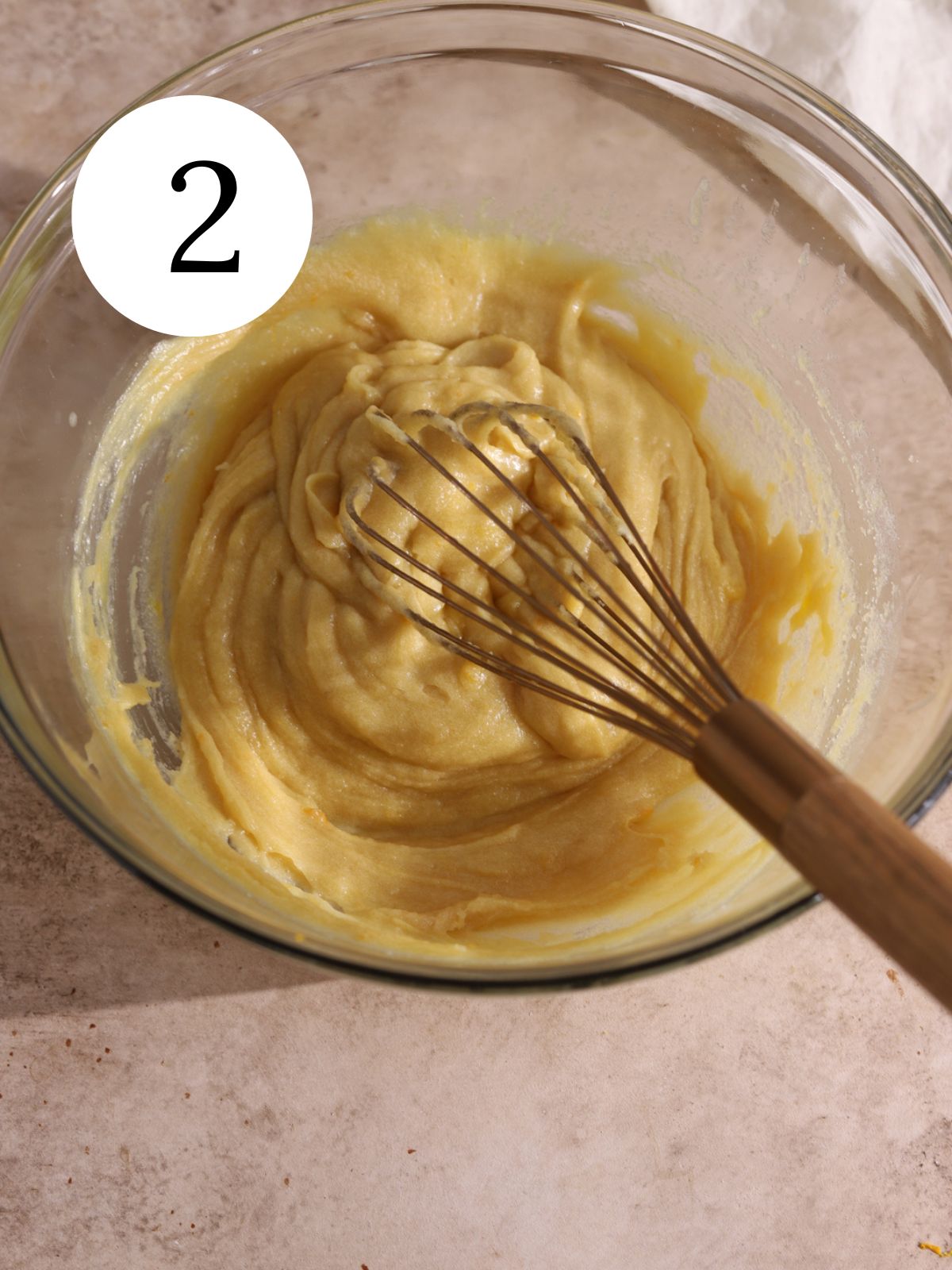 A whisk mixing cookie dough in a large glass mixing bowl.