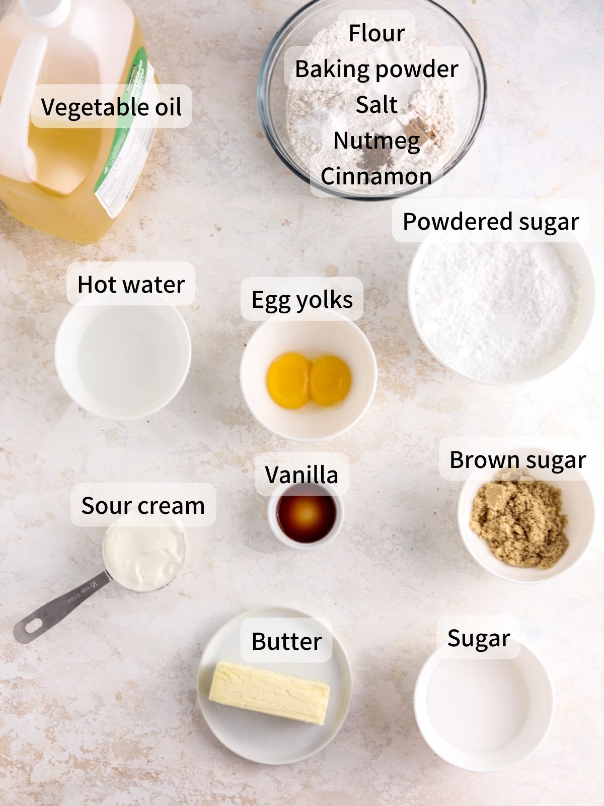 Labeled ingredients needed to make sour cream donuts laid out on a table. 