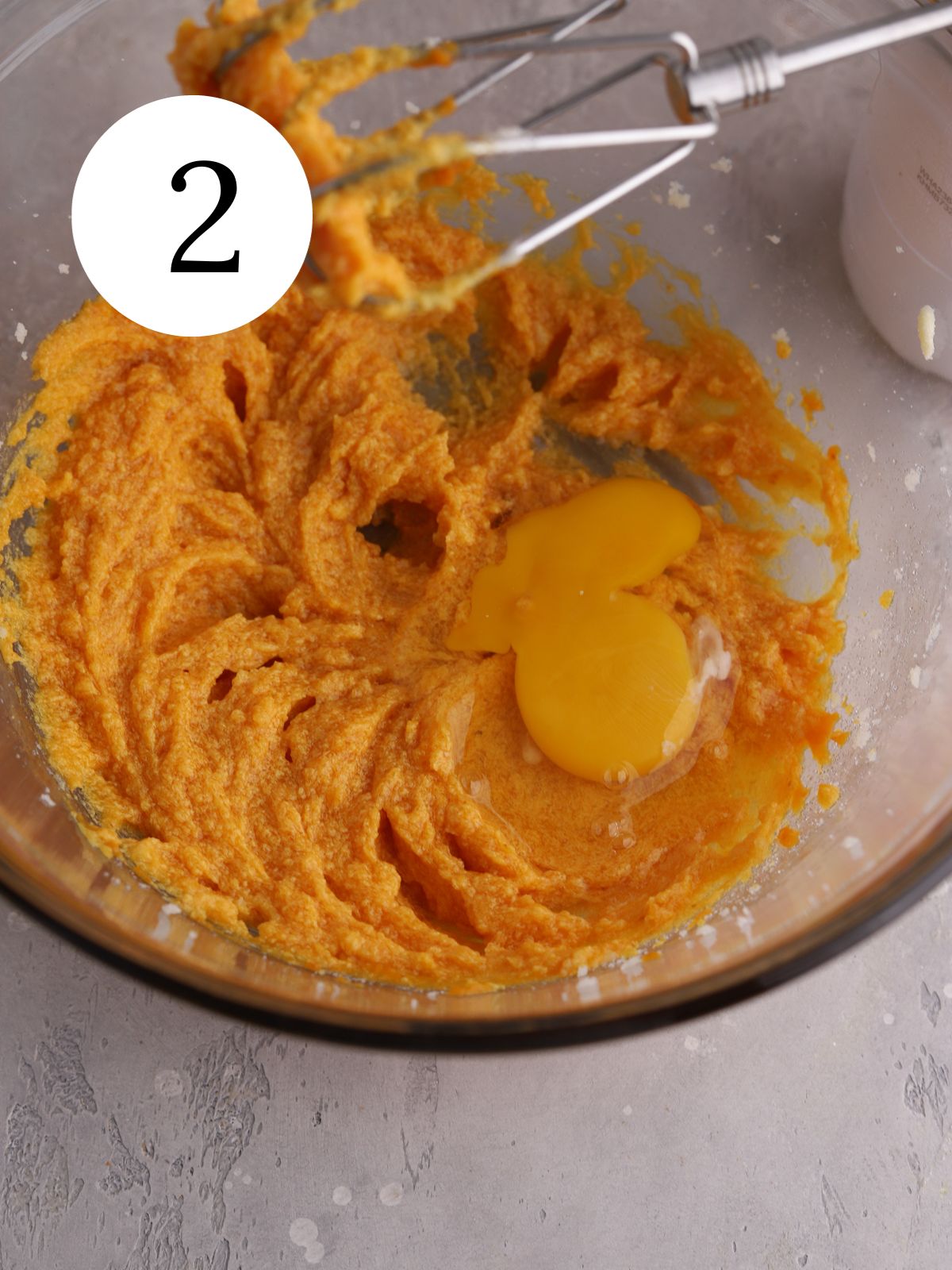 Orange pumpkin cookie dough and an egg on top in a glass bowl.