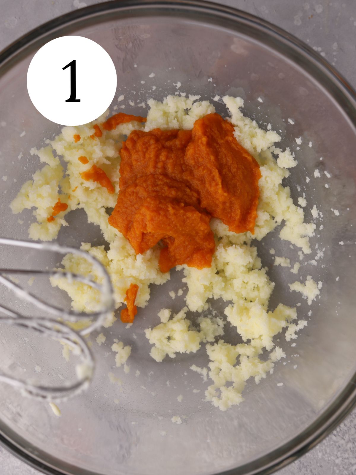 A mixing bowl with pumpkin puree added to creamed butter.