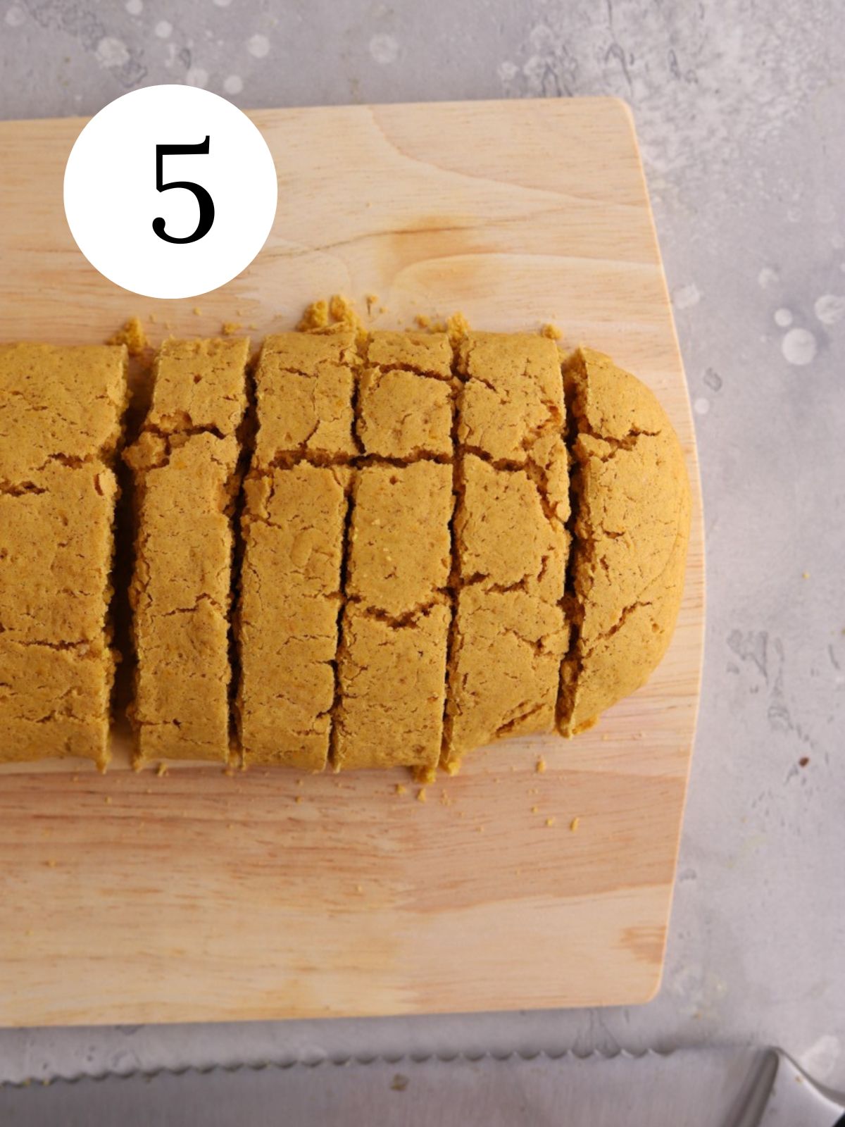 An orange biscotti log on a cutting board and a serrated knife.