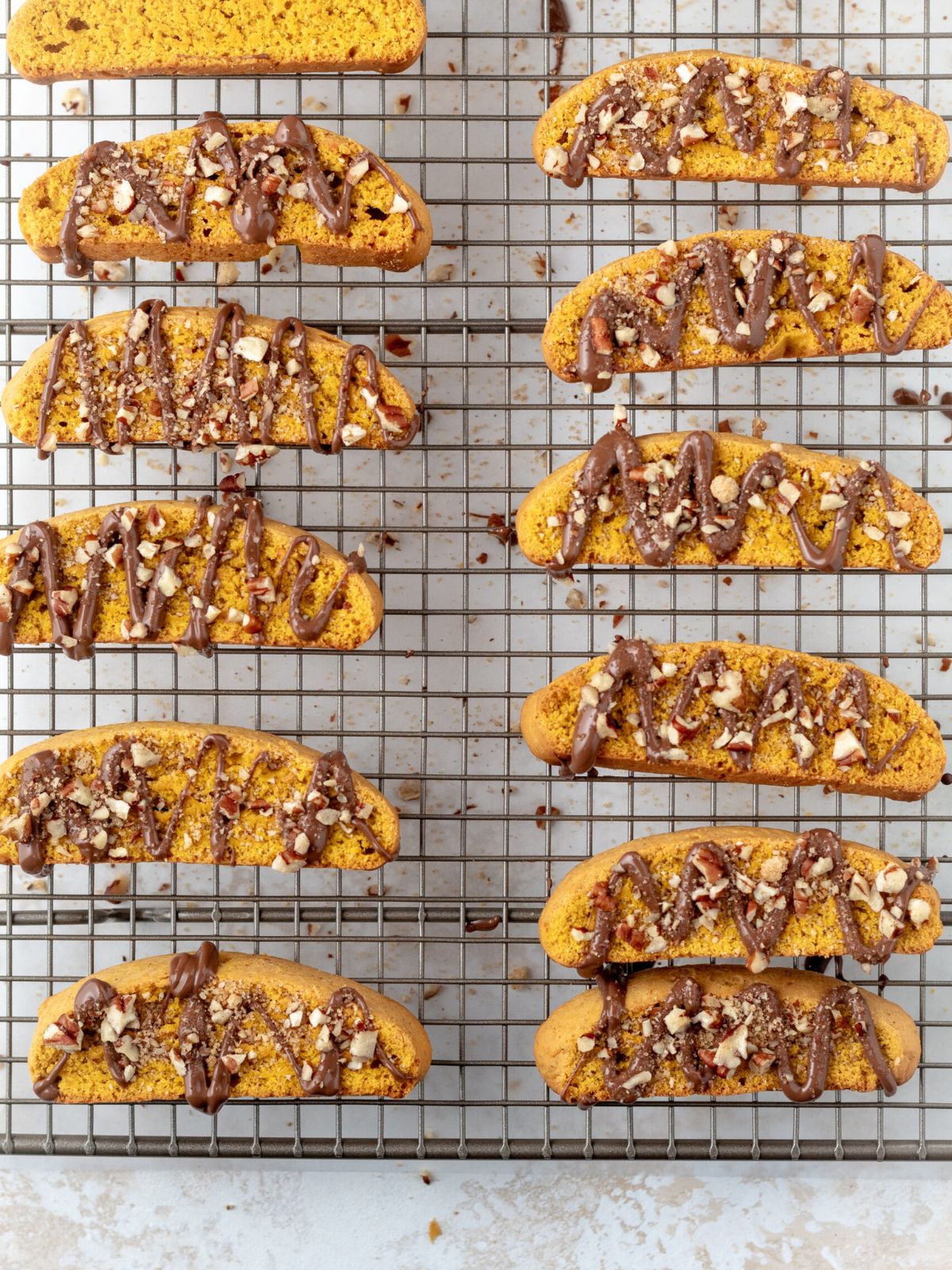Pumpkin biscotti drizzled with chocolate and topped with chopped nuts on a rack.
