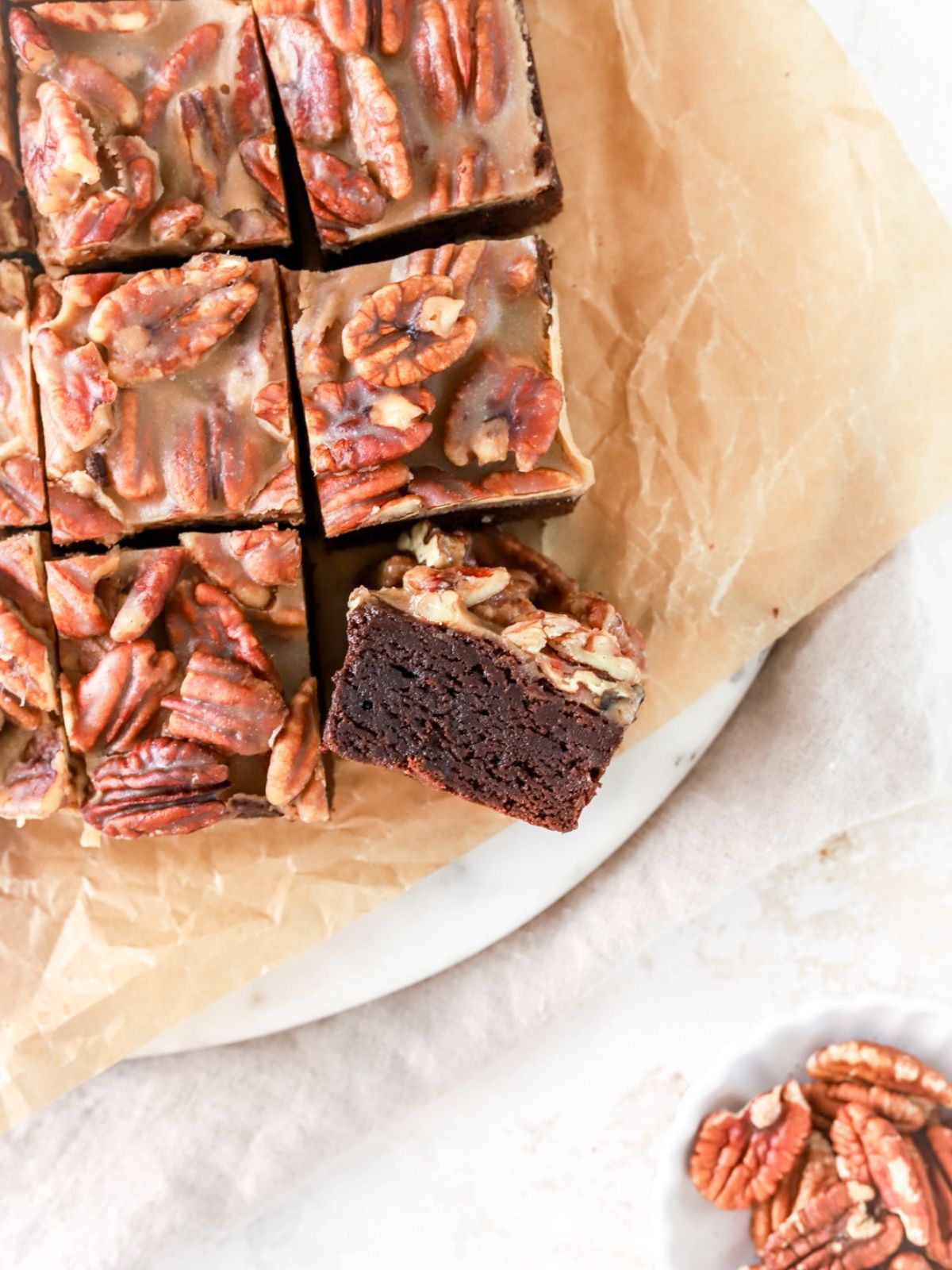 Chocolate brownies with caramel pecans on top and a bowl of pecans. 