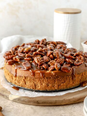 Cheesecake with caramel pecans set on a wooden serving platter.