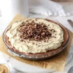 Chocolate pie with peanut butter whipped cream and chocolate shavings in a glass pie plate.