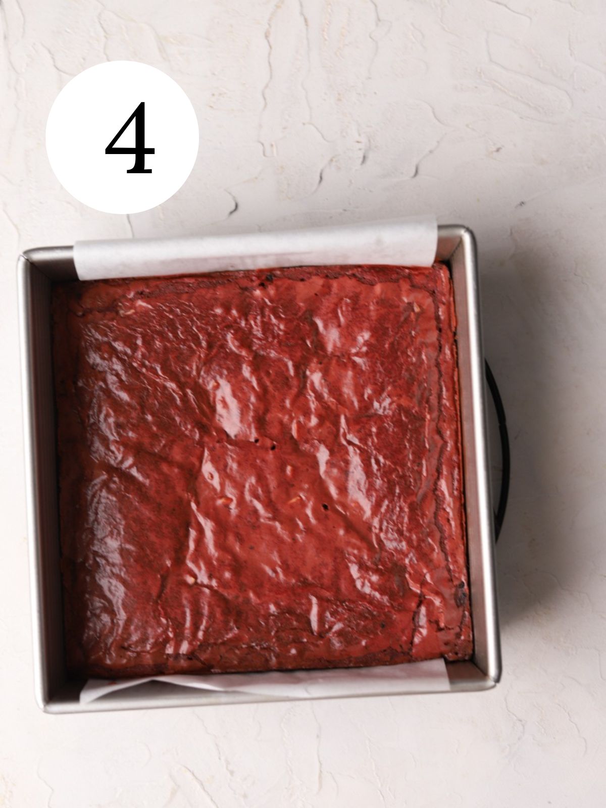 Red colored brownies in a square pan lined with parchment paper.