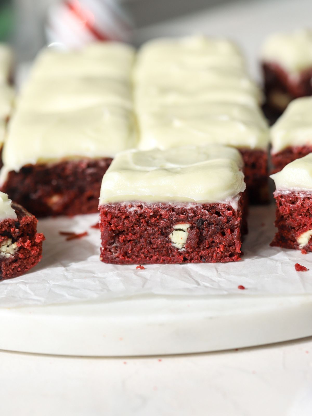 Batch of frosted red velvet brownies on parchment paper.