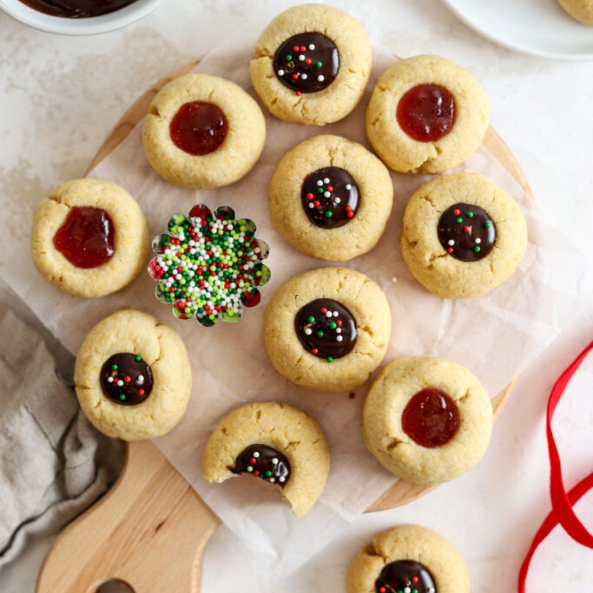 Thumbprint cookies filled with jam and chocolate and a bowl of sprinkles.