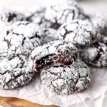 A batch of chocolate cookies coated with powdered sugar on some parchment paper.