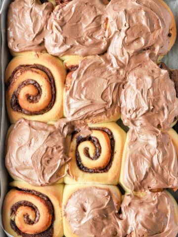 A batch of Nutella cinnamon rolls in a pan with Nutella icing.