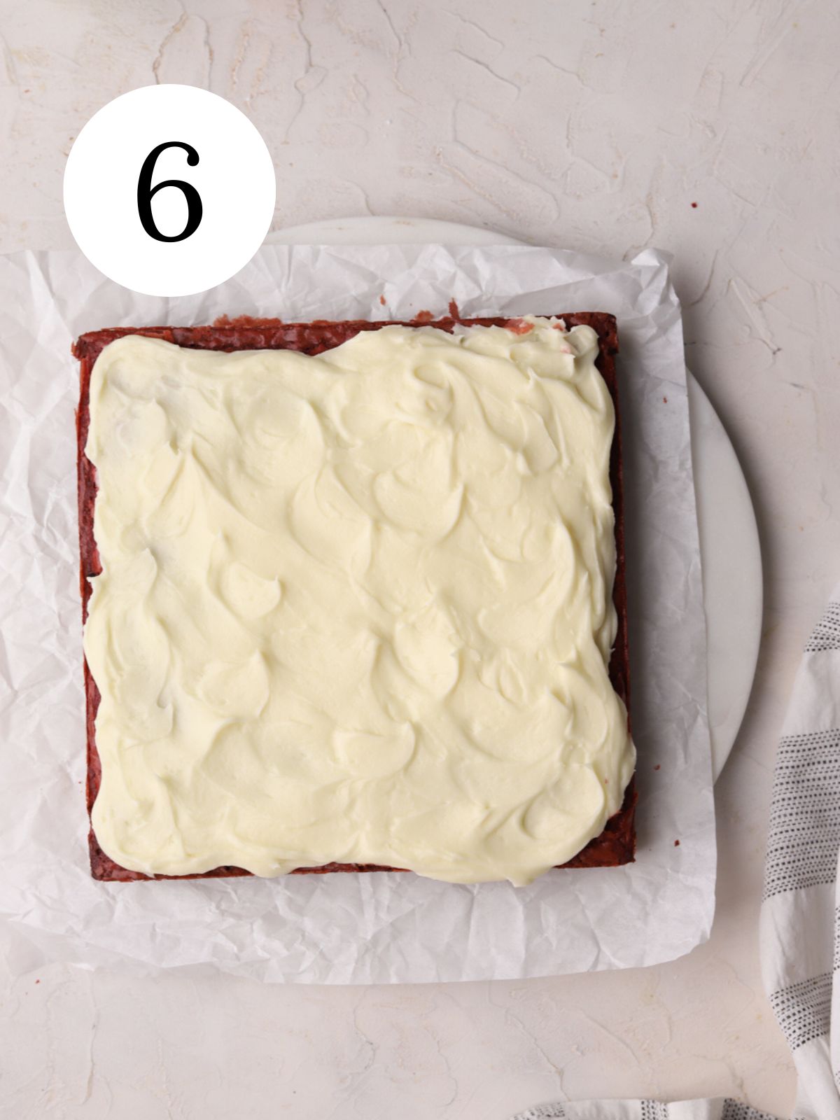 Red velvet brownies with cream cheese frosting on some parchment paper.