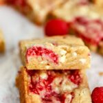 Two blondies with raspberries and white chocolate next to a raspberry.