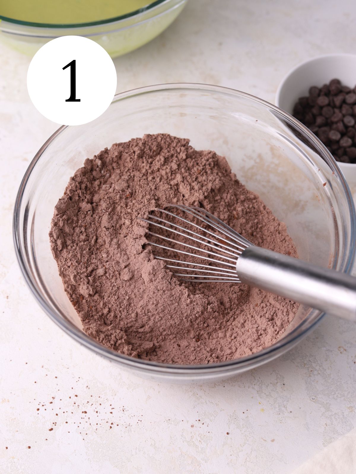 Cocoa powder in a glass mixing bowl with a whisk in it. 