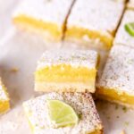 Lime bars cut into squares and topped with powdered sugar and lime slices.