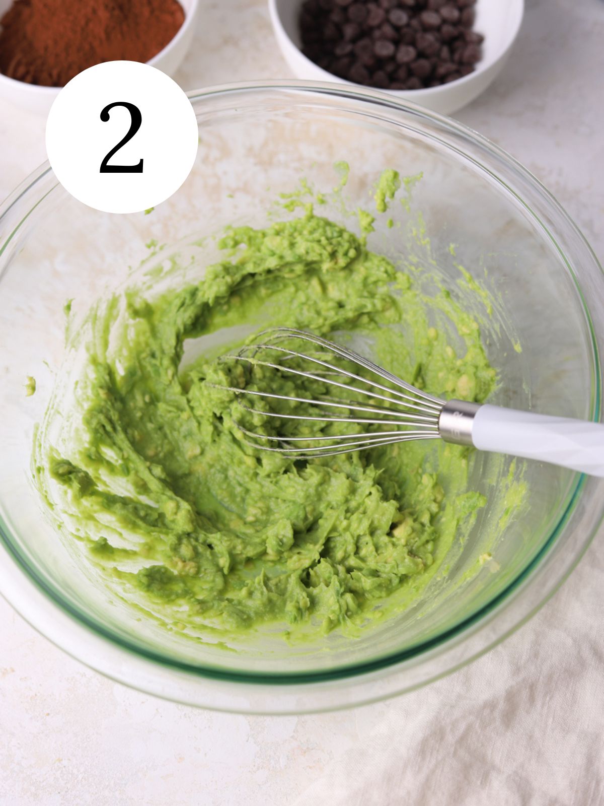 Mashed avocado in a mixing bowl with a whisk.