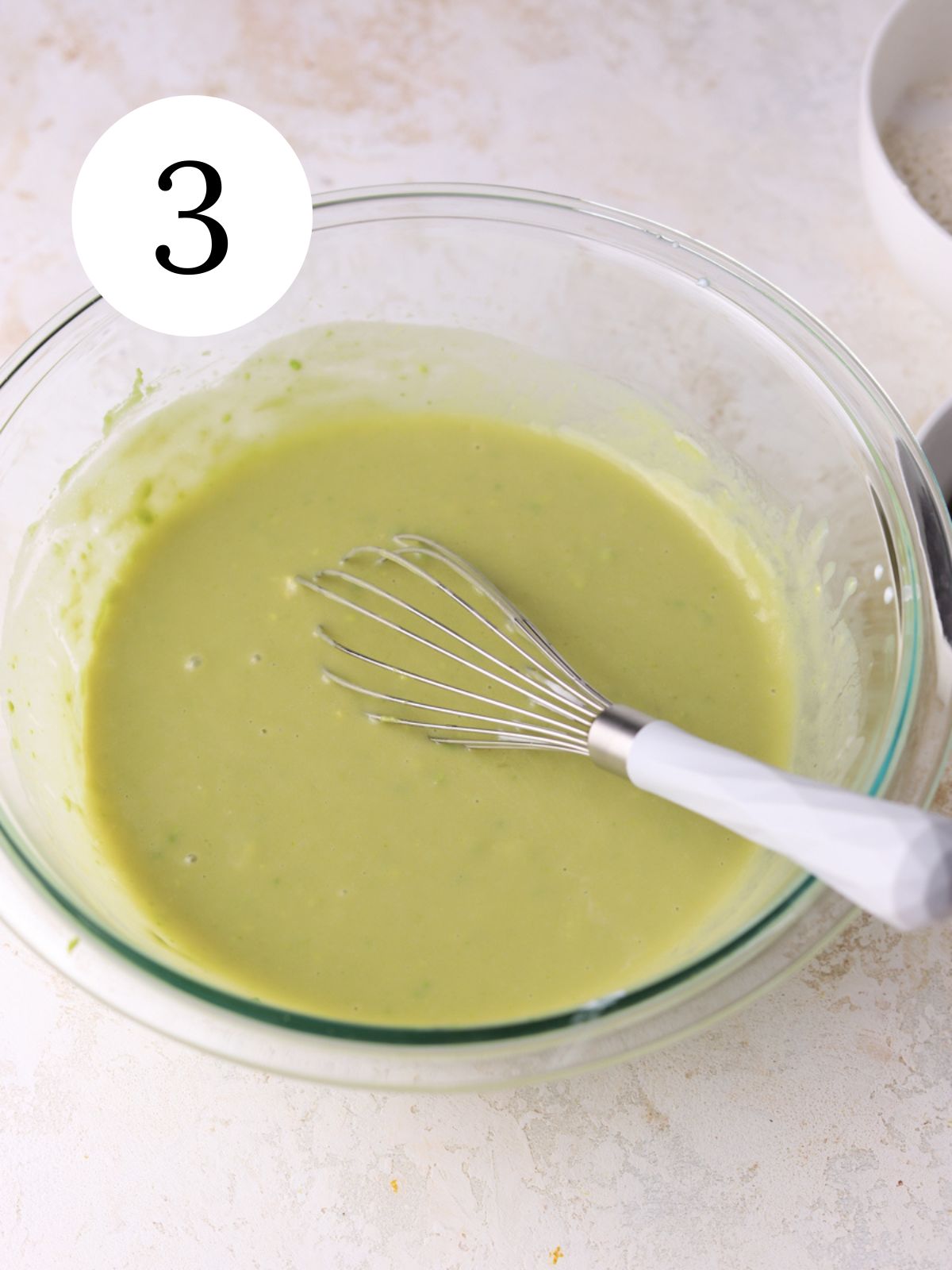 Avocado and other wet ingredients combined with a whisk in a glass bowl.