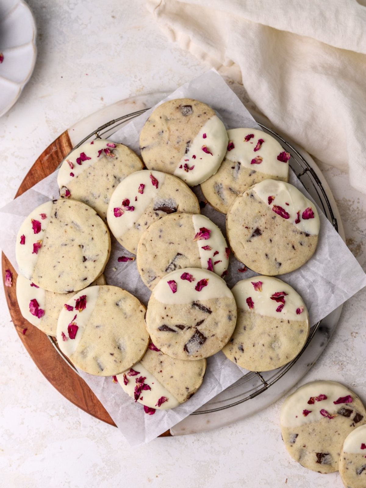 A batch of rose and chocolate cookies dipped in white chocolate on a rack. 