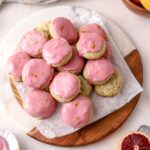 A batch of cookies with pink icing and a half a blood orange.
