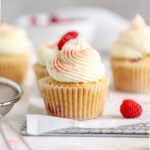A raspberry cupcake with frosting on a rack.