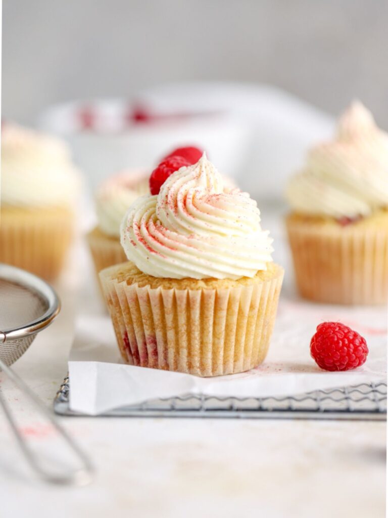 A raspberry cupcake with frosting on a rack.