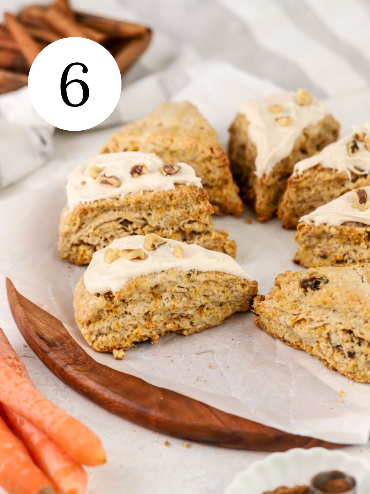 Scones with cream cheese frosting and walnuts on top next to some carrots. 