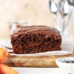 A chocolate loaf cake topped with chocolate glaze next to some carrots.