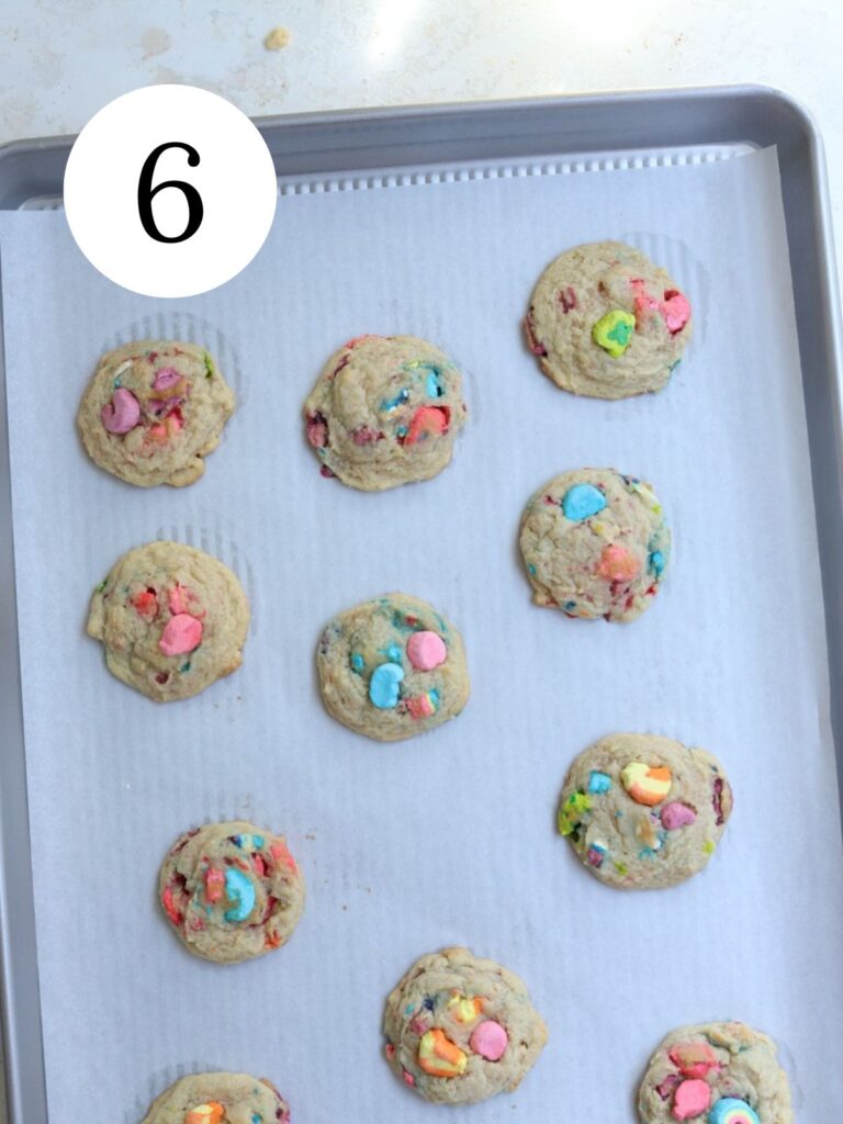 A baking sheet lined with parchment paper with Lucky Charms cookies on it. 