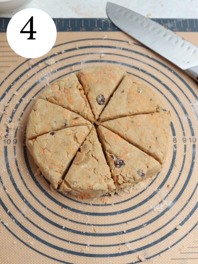 Scones dough in a circle on a pastry mat sliced into triangles next to a knife.