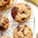 Banana muffins with chocolate chunks on a rack next to some bananas.