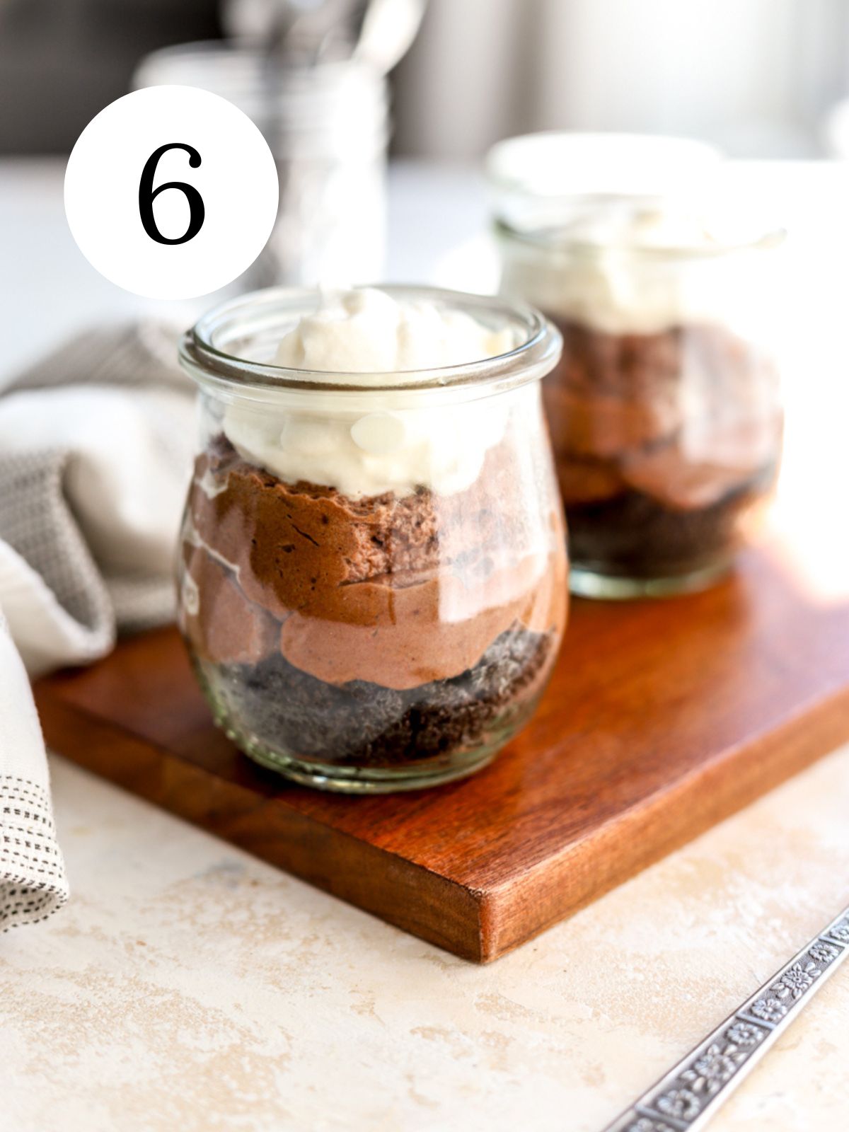 Jars with Oreo crusts, chocolate filling and whipped cream on top on a wooden tray.