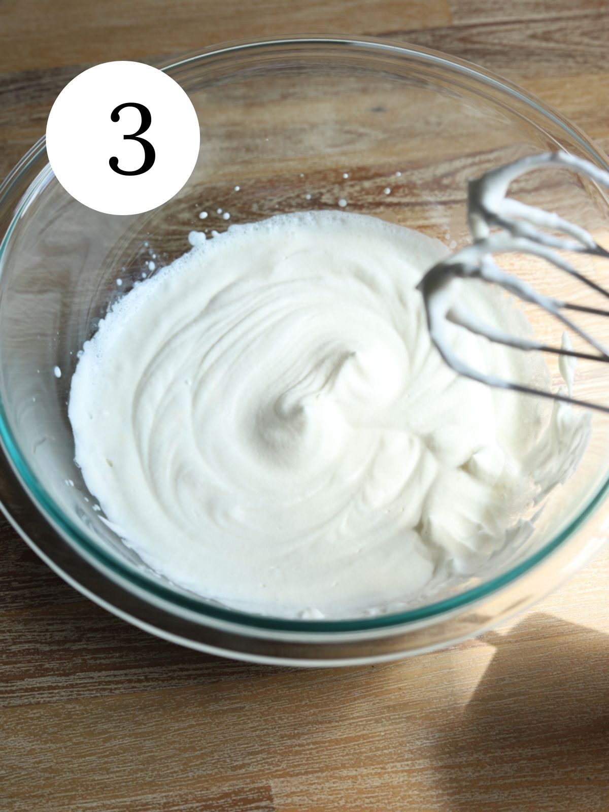 A glass bowl with whipped cream and stiff peaks in it.