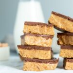 A stack of peanut butter bars with chocolate on top and a milk jug.