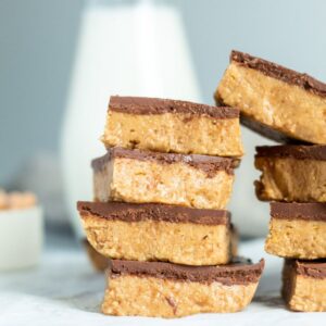 A stack of peanut butter bars with chocolate on top and a milk jug.