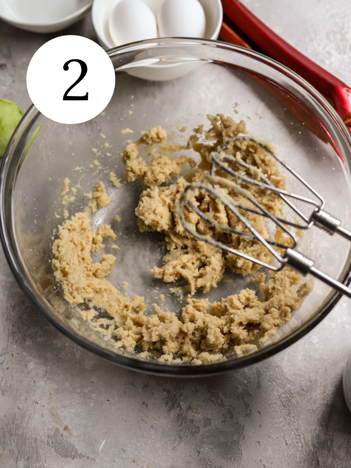 Butter and sugar creamed together in a glass bowl next to some eggs and rhubarb.