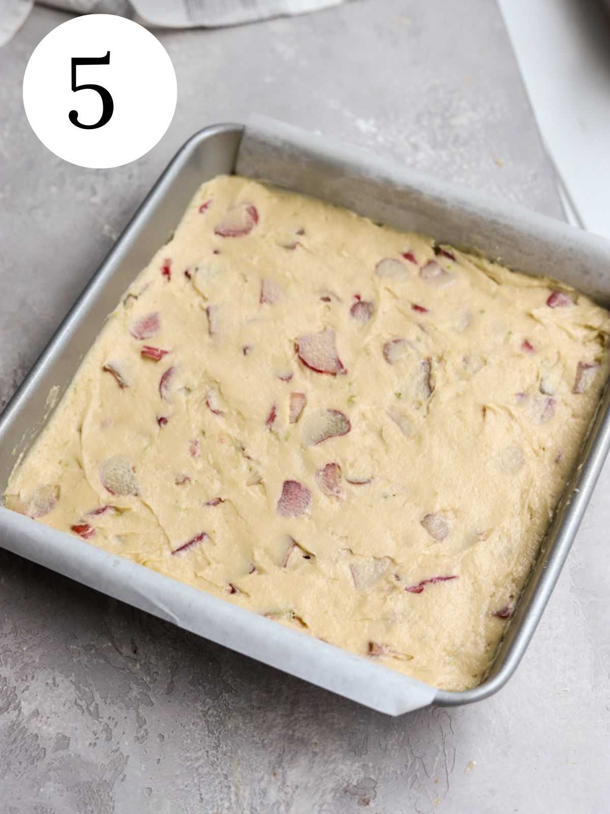 Rhubarb cake batter in a square pan lined with parchment paper.