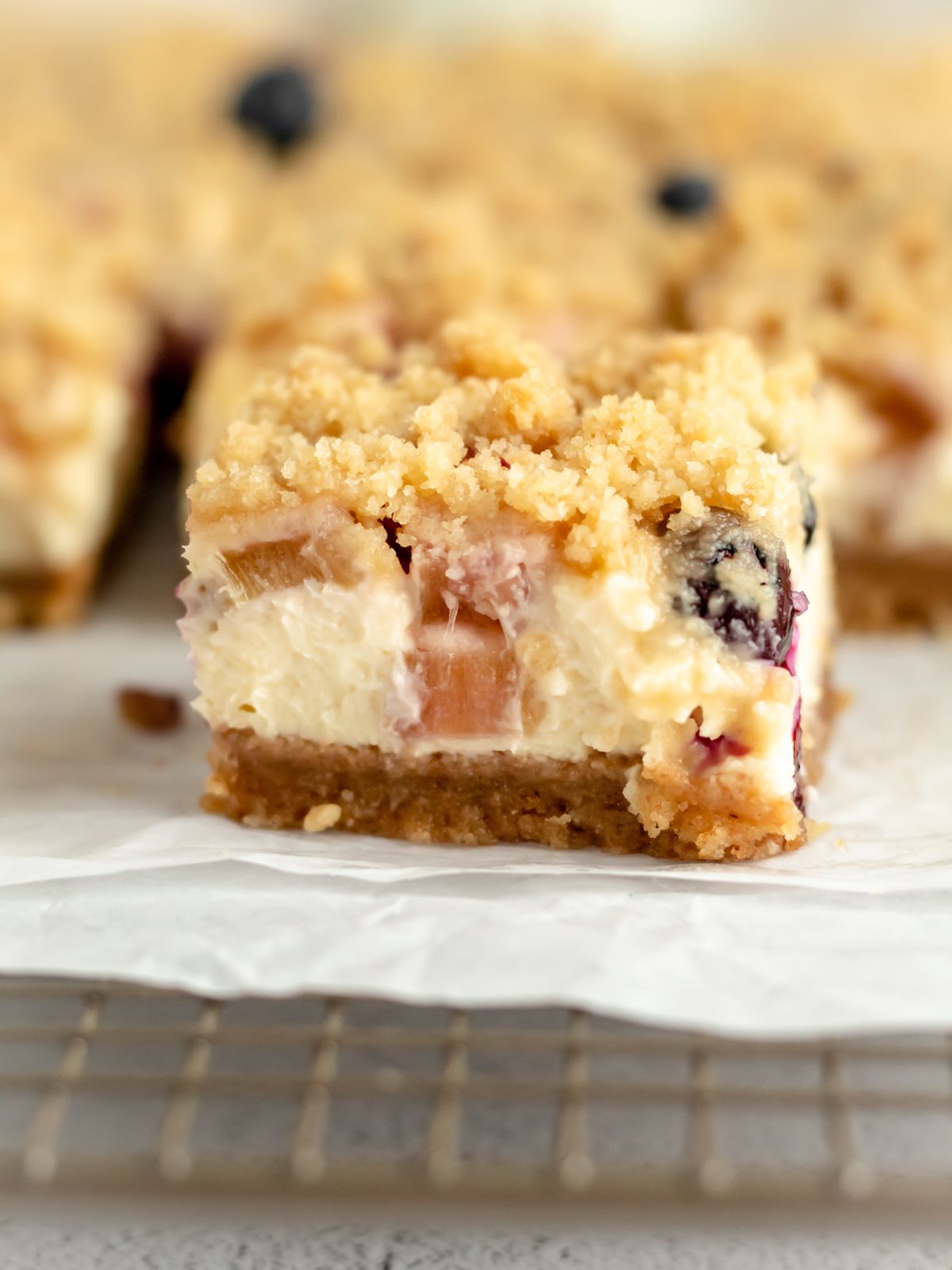 A cream cheese bar with rhubarb and blueberries and a crumble topping. 