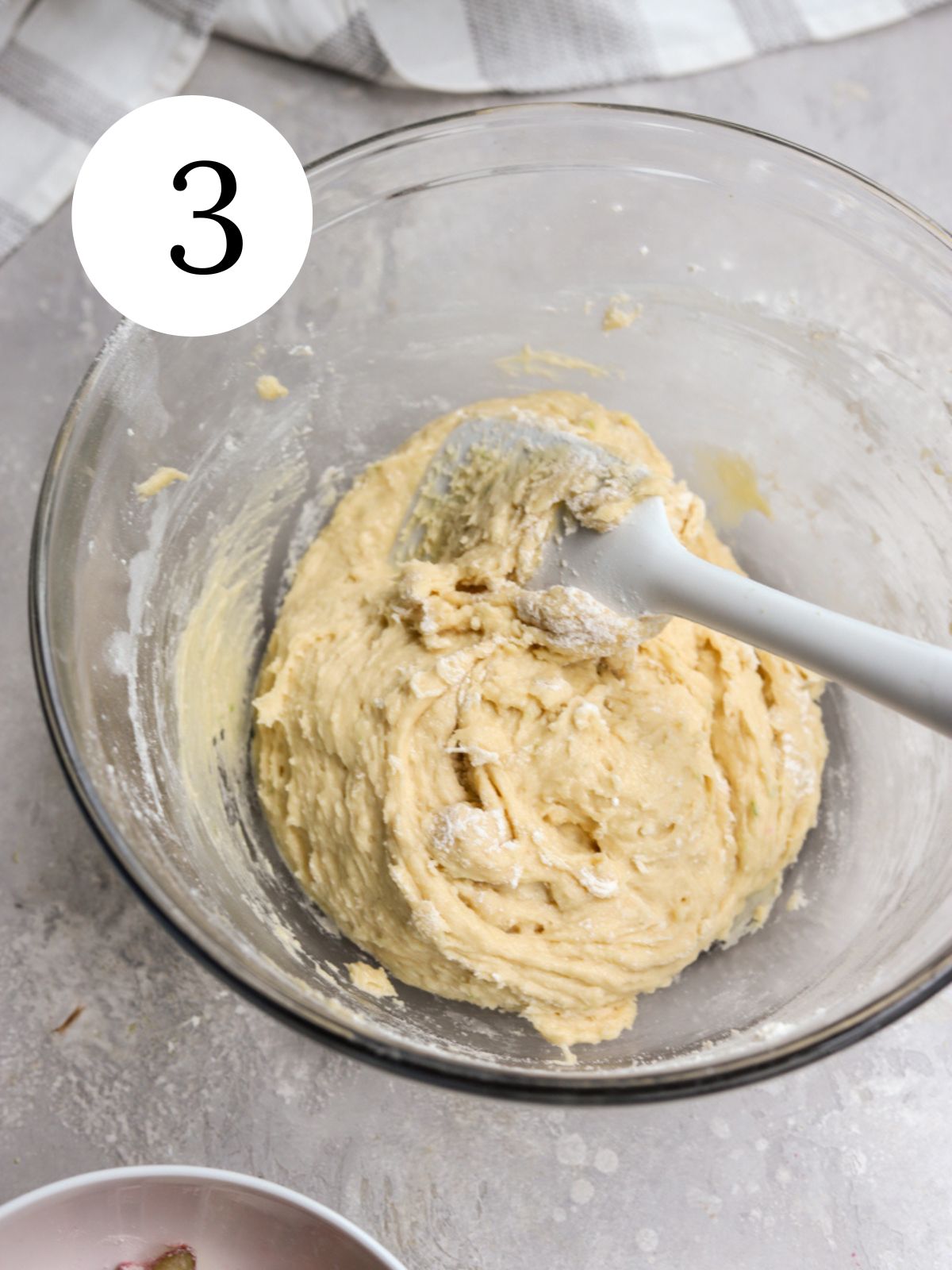 Stirring flour into batter with a spatula in a glass mixing bowl.