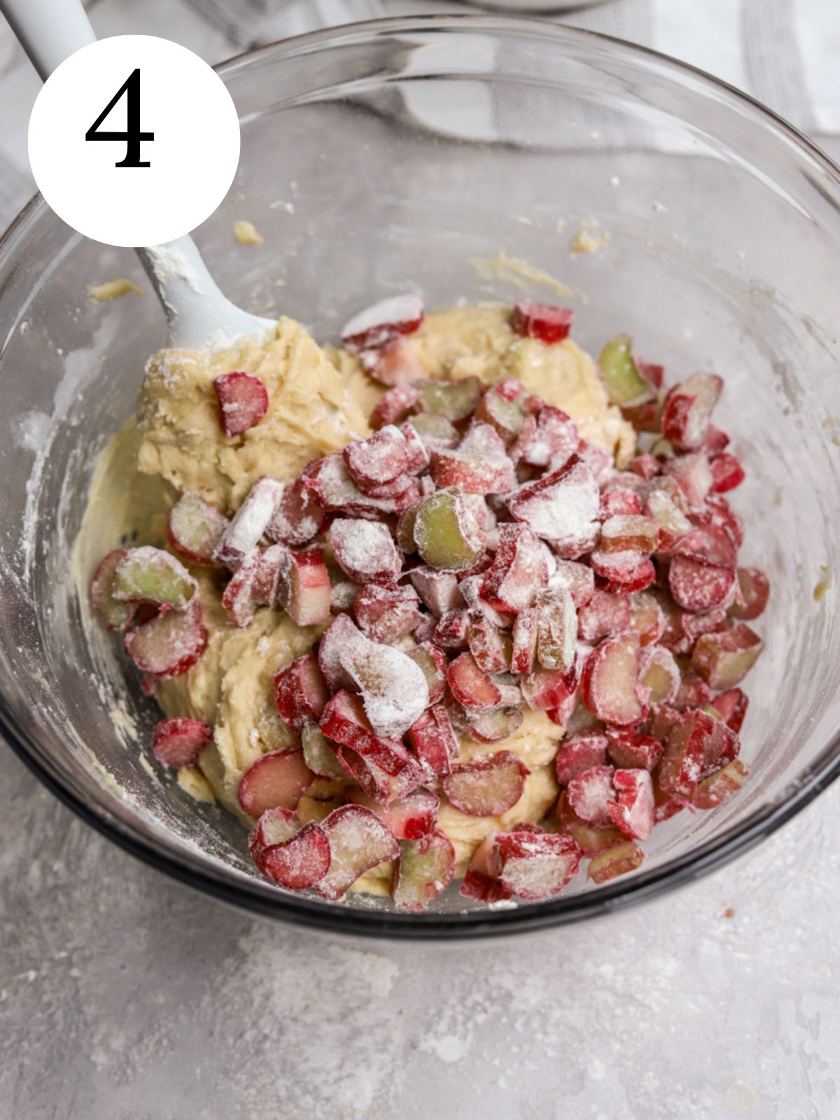 Chopped rhubarb and cake batter in a glass bowl with a spatula.