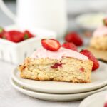 A strawberry scone with pink icing and a berry on top on a plate.