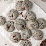 A batch of chocolate chip cookies on parchment paper next to dried hibiscus.