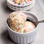 Scoops of sprinkle filled ice cream in a white bowl with a spoon.