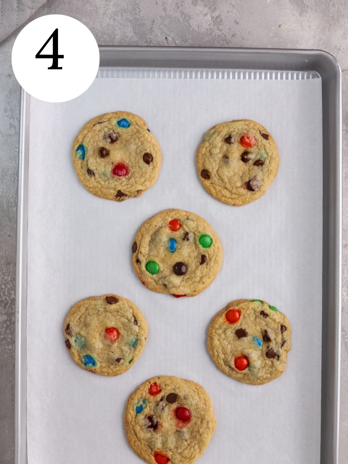 Chocolate chip cookies with M&Ms on a baking sheet lined with parchment paper.