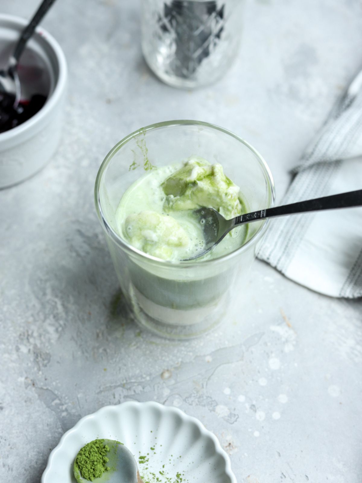 A glass with ice cream and matcha and a spoon in it.
