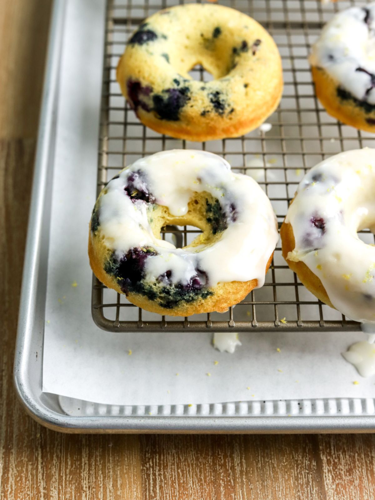 Blueberry donuts with lemon glaze on a baking rack set over parchment paper.