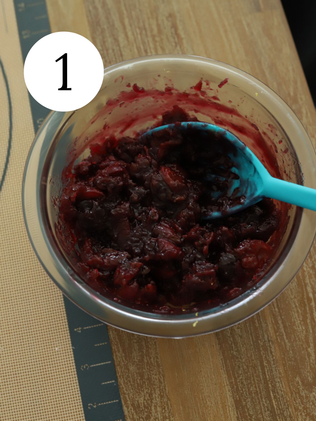 A glass bowl with cherry sauce and a blue spoon.