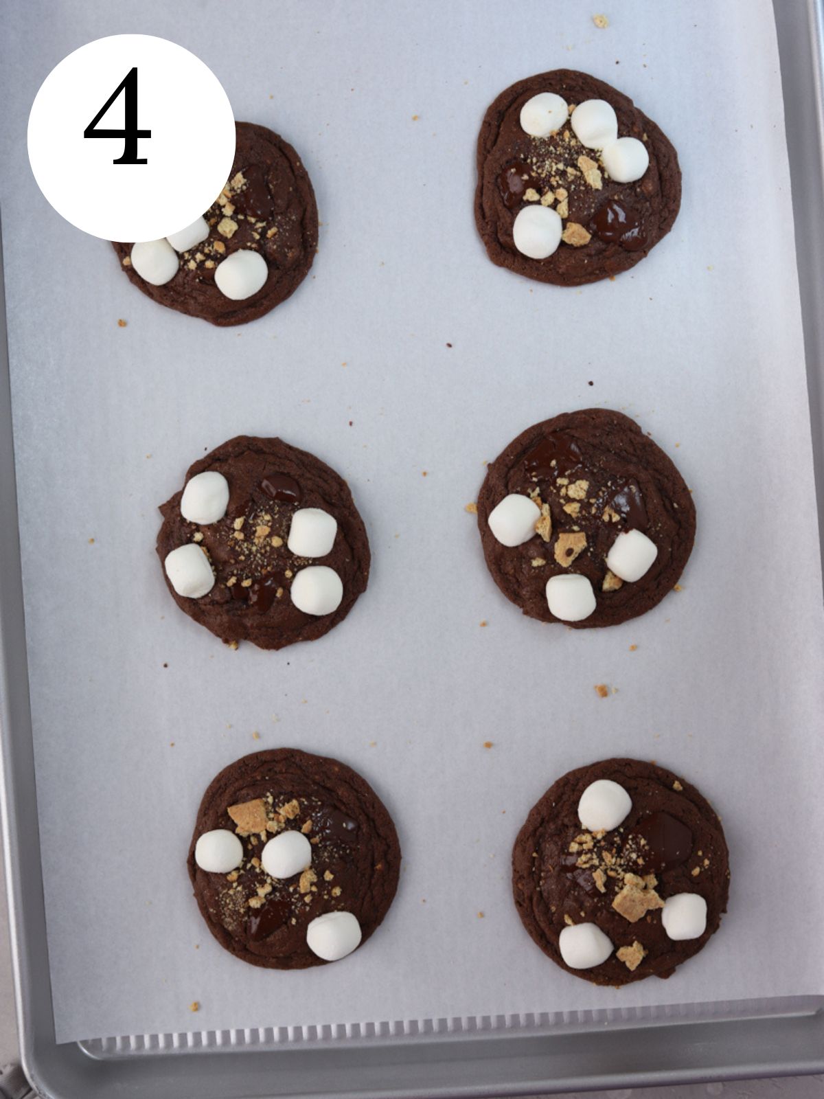 Chocolate cookies with marshmallows and graham cracker crumbs on a baking sheet.