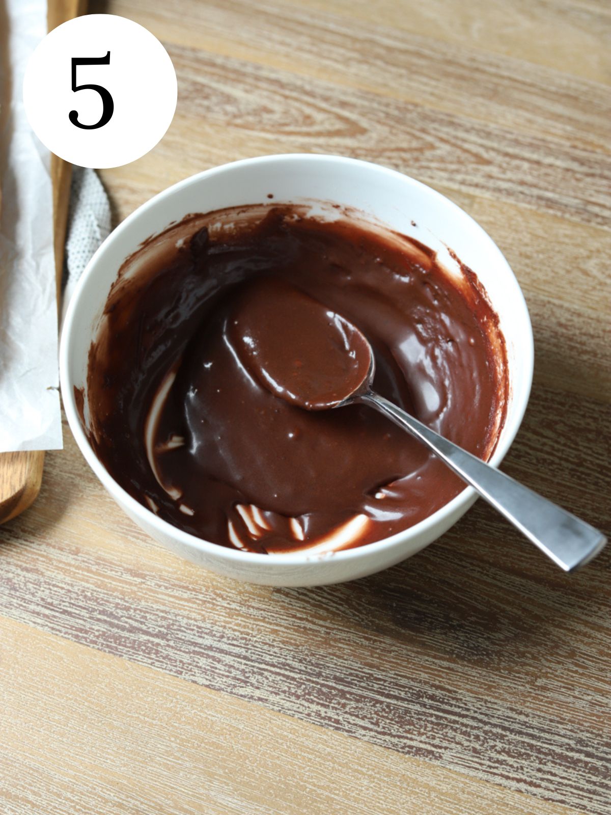 A white bowl with chocolate sauce and a spoon.