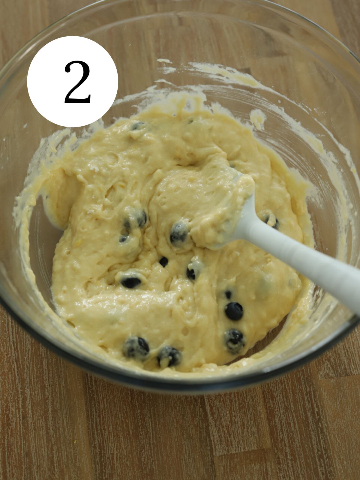 A mixing bowl with blueberry cake batter and a white spatula. 