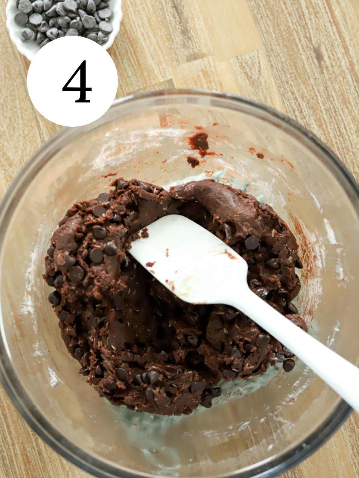 Chocolate chip cookie dough in a bowl with a spatula and a bowl of chocolate chips.